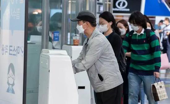 戴口罩的乘客们在首尔车站内进行消毒。新华社图